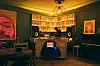 Warm music venue with a central mixing desk, speakers, framed displays, and a person working.