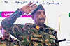 Abdel Fattah al-Burhan in camouflage salutes at an event in Port Sudan as Arabic signs appear in the background.