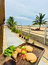 Burgers and fried food on a wooden board overlooking a tropical beach.