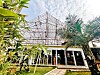 Glass pavilion surrounded by tropical plants beneath a large geometric steel canopy.