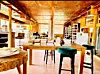 Rustic indoor space with wooden tables, stools, shelves, and warm sunlight.