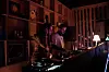 A man and a woman are standing behind turntables at night, both wearing headphones and DJing.