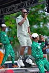Singer performs with dancers in green outfits on an outdoor stage.