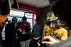 Group of rappers gathered indoors near a barred window, with cables and equipment in the foreground, mics in hand.
