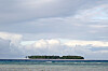 Mnemba Island sits on the horizon beyond shallow blue water beneath a cloudy sky.