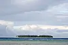 Mnemba Island sits on the horizon beyond shallow blue water beneath a cloudy sky.