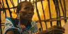 A woman wears beaded earrings and a blue patterned wrap while seated inside a traditional structure in a still from the Kenyan film One Woman One Bra.