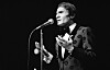 Abdel Halim Hafez sings into a microphone on a dark stage in a black-and-white photograph.
