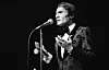 Abdel Halim Hafez sings into a microphone on a dark stage in a black-and-white photograph.
