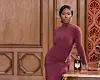 Ivie Ani wears a burgundy dress and stands beside a drinks table in an ornate, wood-paneled room.