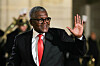 Smiling Aliko Dangote in a black suit and red tie waving at an evening event.
