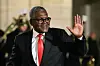 Smiling Aliko Dangote in a black suit and red tie waving at an evening event.