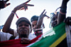 A group of people raises their hands behind the red, white, green, yellow, and black South African flag.