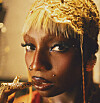Close-up portrait of a person wearing a gold headpiece and holding a golden accessory near their lips.