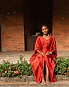 Woman in a red outfit seated beside flowers outside a brick building.