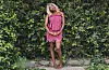 Celeste Ojatula in a pink striped dress standing against a leafy hedge.
