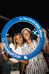 Two smiling women pose inside a blue branded circle at an indoor event.