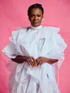 Judith Sephuma in a voluminous white ruffled dress posing against a pink background.