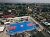 Aerial view of a blue and red basketball court surrounded by dense urban housing.