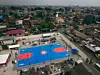 Aerial view of a blue and red basketball court surrounded by dense urban housing.