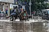 Passengers travel by horse-drawn cart through a flooded Dakar street as cars wait nearby.