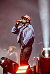 Male singer in a red cap performs into a microphone on a hazy, brightly lit stage.