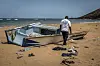 An IOM worker examines a damaged boat on a sandy beach near Obock, Djibouti.