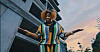 Person in a colorful patterned outfit stands with arms outstretched beside a modern building.
