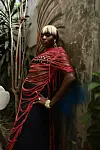 Woman in a red draped wrap and black dress poses beside tropical plants and a textured wall.