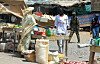 Vendor stands beside sacks and produce at a busy open-air market in Abyei.