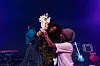 Two women are sticking plastic flowers to a microphone on a stage.