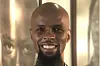 A bald Black man with a beard smiles brightly for a close-up portrait.