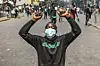 A young man with a mask partially covering his face kneels with his hands up, holding rocks, during protests against police brutality at the Central Business District in Nairobi, Kenya.