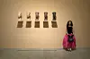 Sara Elmessiry wearing a black shirt and pink skirt, standing in front of five Nefertiti busts in different skin colors ranging from beige to dark brown.