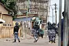 Members of the Togolese Gendarmerie in riot gear and machine guns facing away from the camera on an empty street