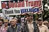 Group of white South African Trump supporters attend a pro-Trump rally, holding a large banner that reads “Mr. Donald Trump, Thank You VERY MUCH” with American flag graphics.