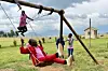 Children playing on a swing in a grass field.