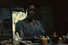 A still from the film of the actress Wunmi Mosaku in a dimly-lit setting, lighting a candle.