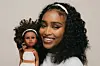 A Black woman holds up a Black doll that resembles her.