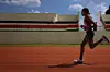 Faith Kipyegon running on a track in Kenya wearing athletic gear with empty stadium stands in the background.