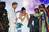 A photo of Prince Harry and Meghan Markle smiling as they receive outfits gifts from a woman.
