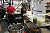 Four women standing in the kitchen, facing the restaurant. Behind them, several large pots filled with sauces on the counter.
