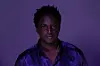 Ugandan artist Joshua Baraka poses in a purple shirt.