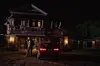 An image from the film The Weekend of a man at night standing next to a car in front of a house.