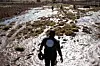 Rescue workers walk across a flooded and muddy field in a rural area.
