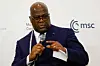 Democratic Republic of Congo (DRC) President Felix Tshisekedi, a bald man in a navy blue suit and glasses speaks into a microphone while gesturing with his hand during a formal conference, with a white backdrop displaying the MSC logo behind him.