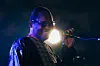 A close-up of Malian singer Amadou Bagayoko singing onstage, drenched in a blue light.