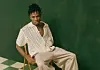 Nigerian singer Joeboy sits on a chair posing in a green room.
