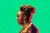 A side portrait photo of Chimamanda Ngozi Adichie in braided hair and spiral earrings, wearing a top made with brown patterned African prints.