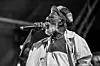 A black and white photo of Jamaican reggae musician singing into a microphone.